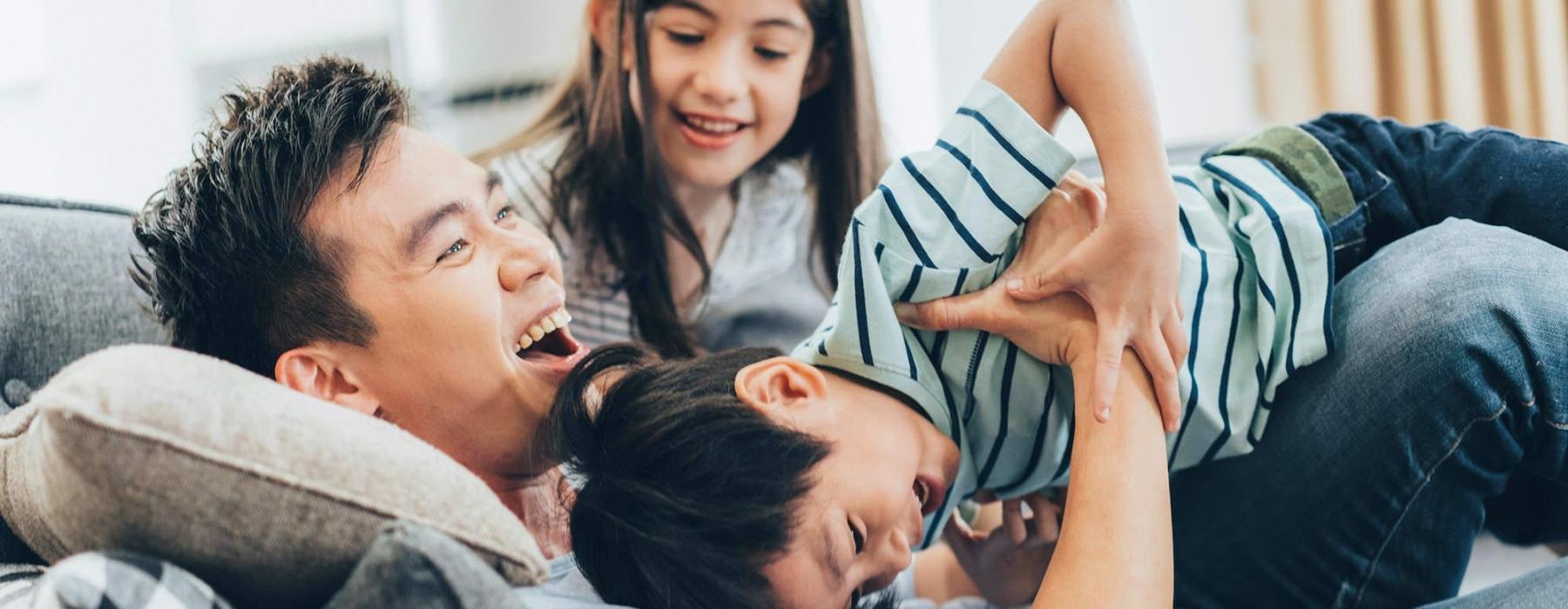 father plays on a couch with his young children